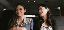 two women are sitting in the back seat of a car .