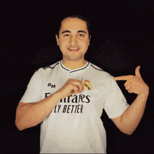 a man wearing a white emirates fly better shirt points to his chest