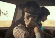a person is sitting in the back seat of a car covering their mouth with their hand .