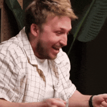 a man in a plaid shirt is laughing while holding something in his hand