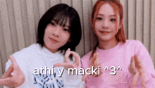 two girls are standing next to each other and making a heart shape with their hands .
