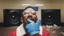 a man wearing glasses and a blue glove has his finger in his mouth