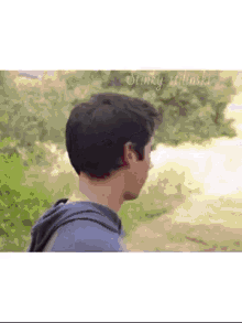 a man in a blue hoodie is standing on a dirt path .