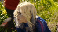 a woman with blonde hair is standing in the grass with a disney logo on the bottom right