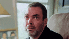 a man with a beard is sitting in a chair in front of a window .