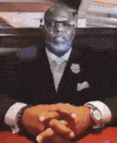 a man in a suit and tie is sitting with his hands folded