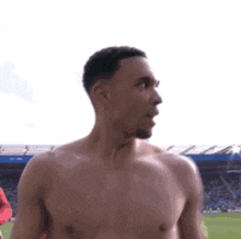 a shirtless man is standing on a soccer field and looking at the camera .