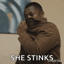 a man in a brown jacket covering his face with his jacket and the words she stinks