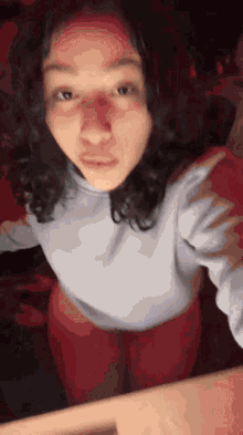 a woman in a white sweater and red pants is taking a picture of herself .