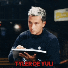 a man holding a notepad with the name tyler de yuli written on the bottom