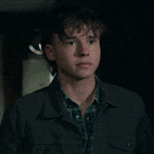 a young man wearing a plaid shirt and a gray jacket