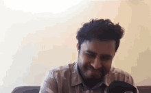 a man with curly hair and a beard is sitting on a couch and laughing .