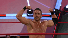 a shirtless wrestler flexes his muscles in a wrestling ring