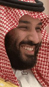 a man with a beard wearing a red and white checkered scarf smiles