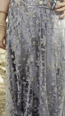 a woman is wearing a gray dress with embroidered flowers and leaves .