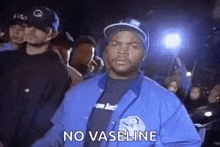 ice cube is wearing a blue jacket and a black shirt and is standing in front of a crowd .