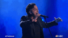 a man singing into a microphone with a nbc logo in the corner