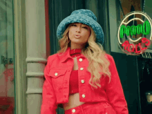 a woman wearing a red jacket and a blue hat stands in front of a neon sign that says o'ream