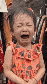 a little girl in a pink dress is crying with her eyes closed .