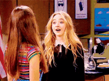 a couple of girls are standing next to each other in a classroom .