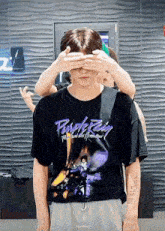 a man wearing a purple rain t-shirt covering his eyes with his hands
