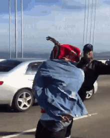 a man in a denim jacket is standing on a highway with a white car behind him