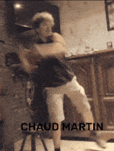 a man in a black shirt and white shorts is standing in front of a fireplace with the words " chaud martin " on the bottom