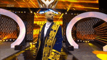 a man in a blue and gold robe is standing on a stage in front of a large screen .