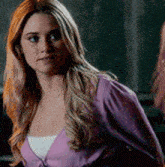 a woman with long blonde hair is wearing a purple sweater and a white tank top .