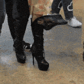a woman wearing a pair of black high heeled boots holds a black bag over her knee