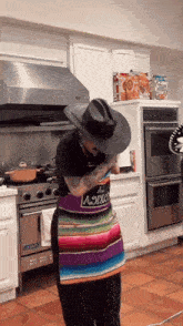 a person in a kitchen wearing a cowboy hat and an apron that says aoixo