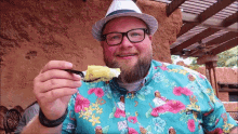 a man wearing a hat and glasses is holding a piece of cake