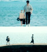 a man carrying a cardboard box walks by a woman carrying a black bag