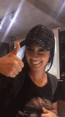 a woman wearing a black hat is smiling and giving a thumbs up .