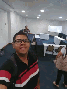 a man wearing glasses takes a picture of himself in an empty conference room