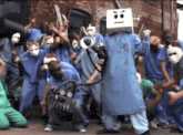 a group of people wearing masks and scrubs are standing around a man with a box on his head that says " i "