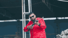a man in a red jacket and sunglasses is holding a gun in a warehouse .