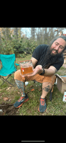 a man with a beard is sitting in the grass and holding a glass of beer