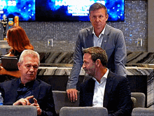 a group of men are sitting in a room with a sign on the wall that says may 23rd