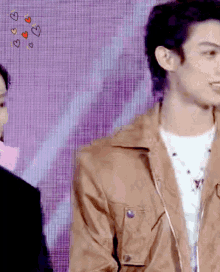 a man in a brown jacket stands in front of a purple background with hearts drawn on it