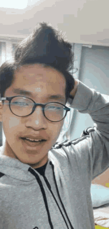 a young man wearing glasses and a gray hoodie holds his hair in a bun