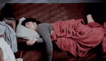 a woman is sleeping on a couch with a red blanket and a pillow .