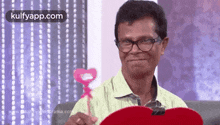 a man wearing glasses is holding a pink heart shaped object .