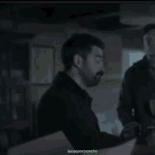 a man with a beard is talking to another man in a dark room with the words locasporponcho below him