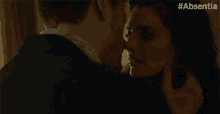 a close up of a man kissing a woman with #absentia written on the bottom right