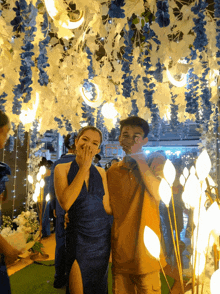 a woman in a blue dress covering her mouth stands next to a boy in an orange shirt