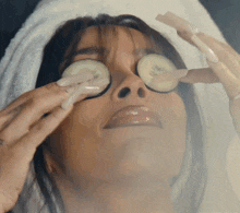 a woman with a towel wrapped around her head is applying cucumber slices to her eyes