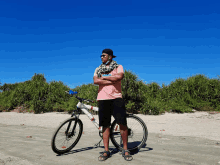 a man in a pink shirt stands next to a bicycle on the beach