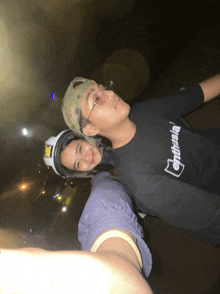 a man wearing a black shirt that says enthusiasia is standing next to a woman wearing a helmet