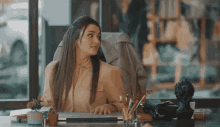 a woman sits at a desk with a laptop and a vase of pencils